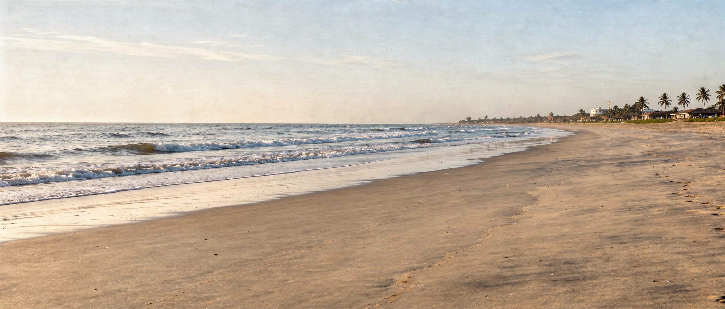 Kothapatnam beach in the early morning: wide flat sand sweeping away, small waves breaking along the shore and a distant line of palms and low rooftops.