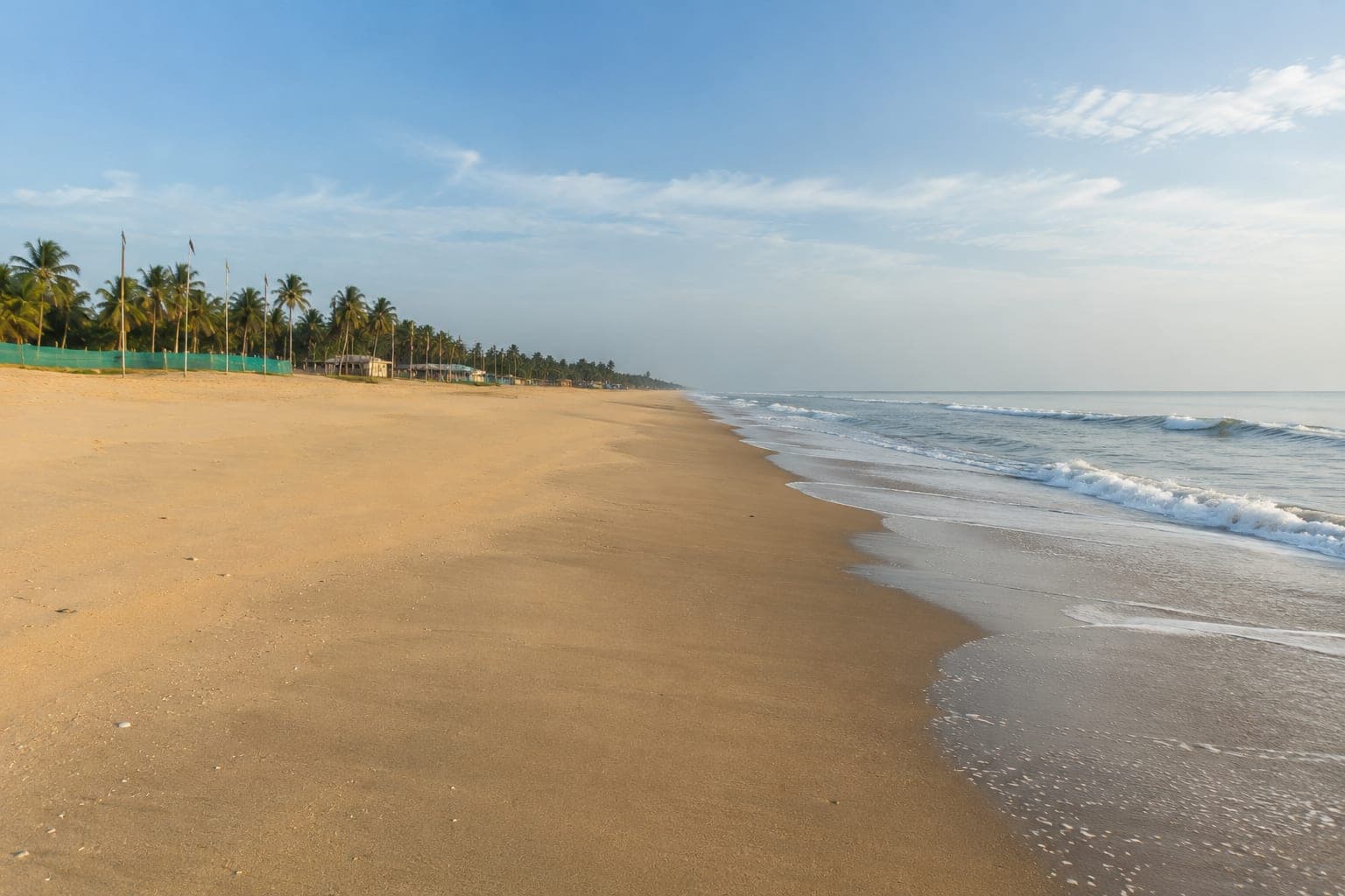 Empty sand at Kothapatnam in the early morning, small waves breaking along the water's edge and a line of palms running back along the dunes.