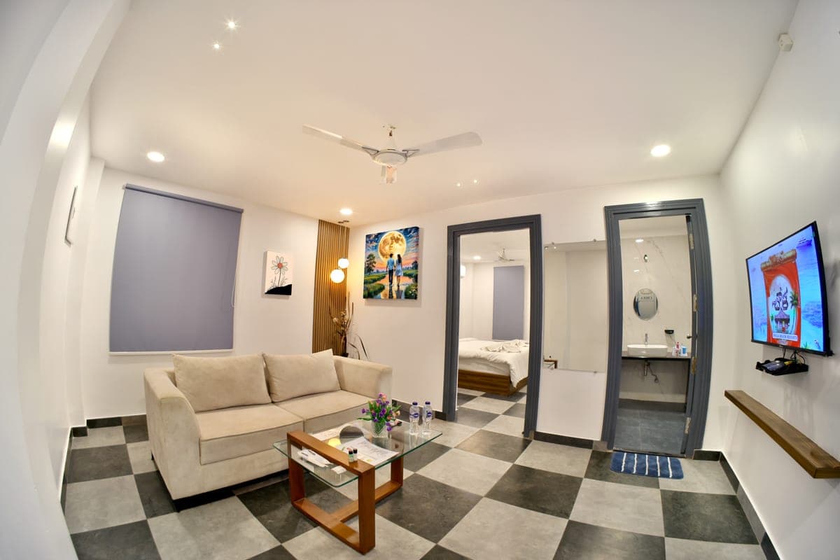 A Deluxe Cottage seen across the living area, with the bedroom doorway on one side and a marble washroom doorway on the other, and a wall-mounted television opposite the sofa.