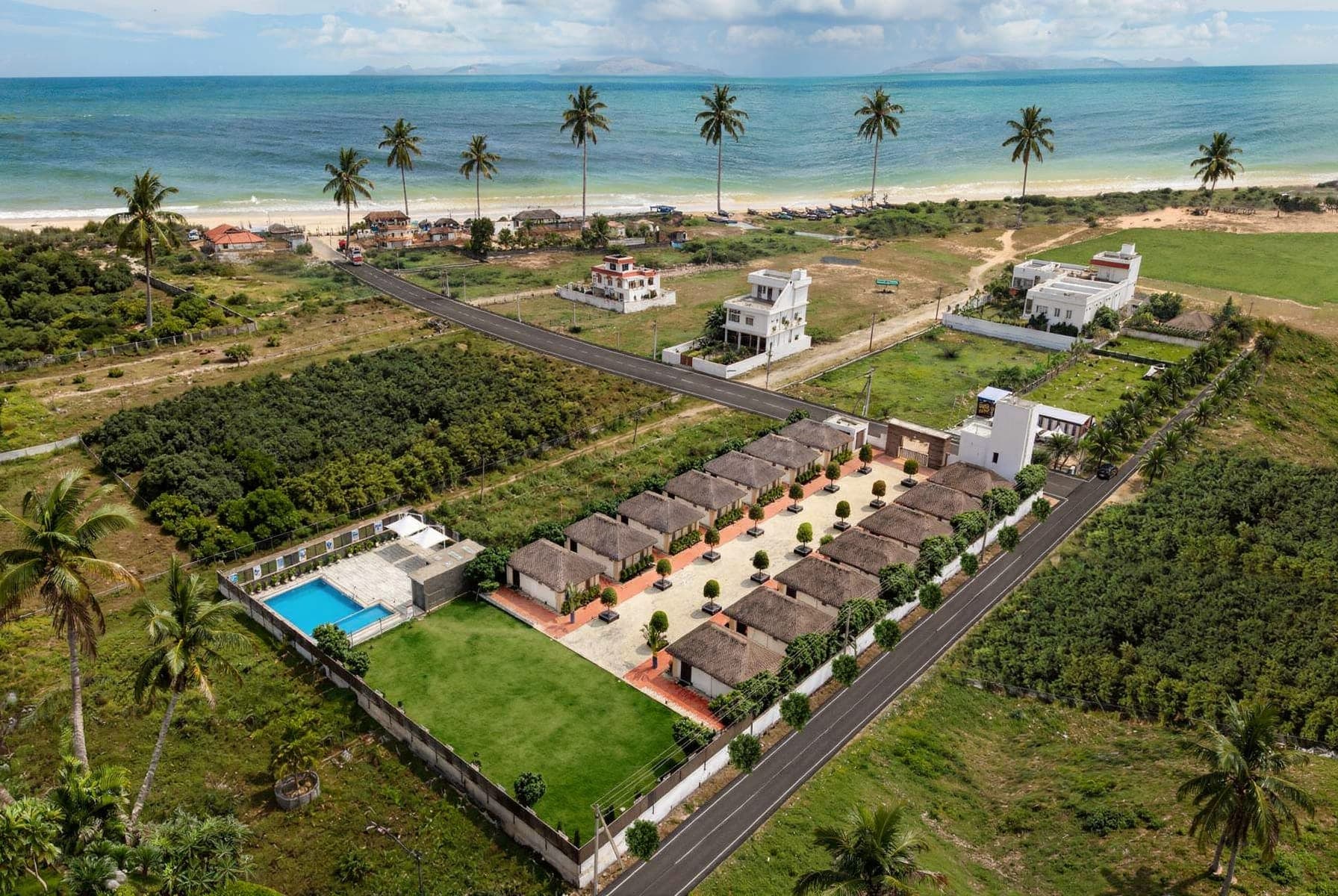 The whole property from the air: fourteen thatched cottages in two rows, the pool and lawn at one end, the coast road and the sea beyond.