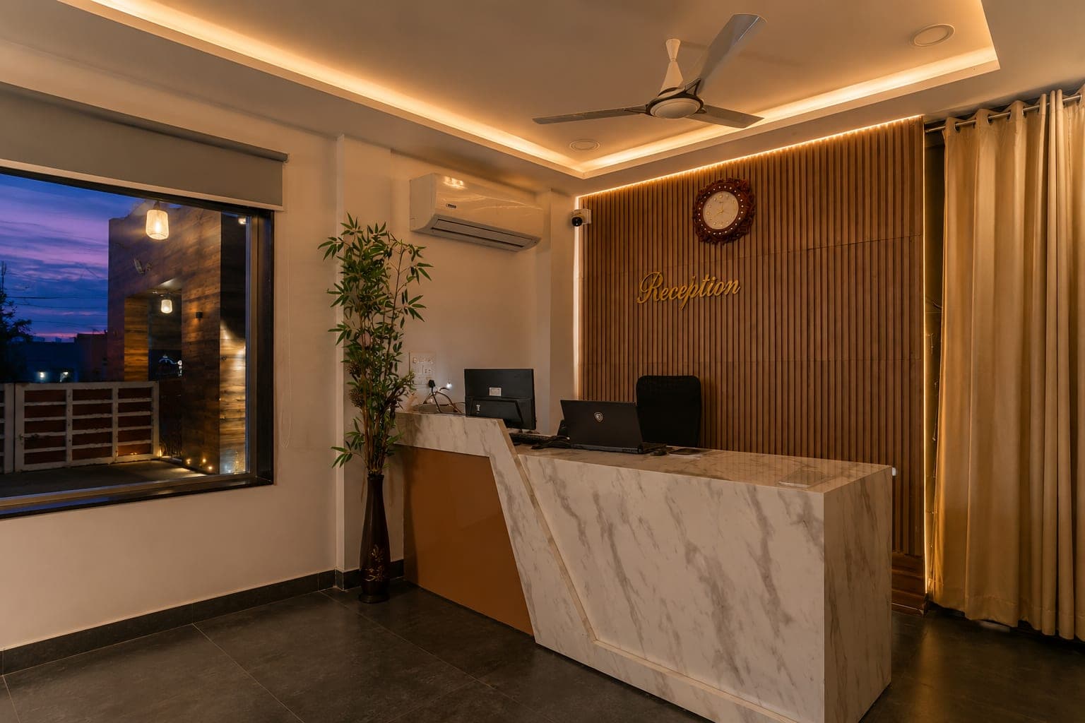 The reception desk in marble and backlit timber under warm cove lighting, dusk in the window behind.