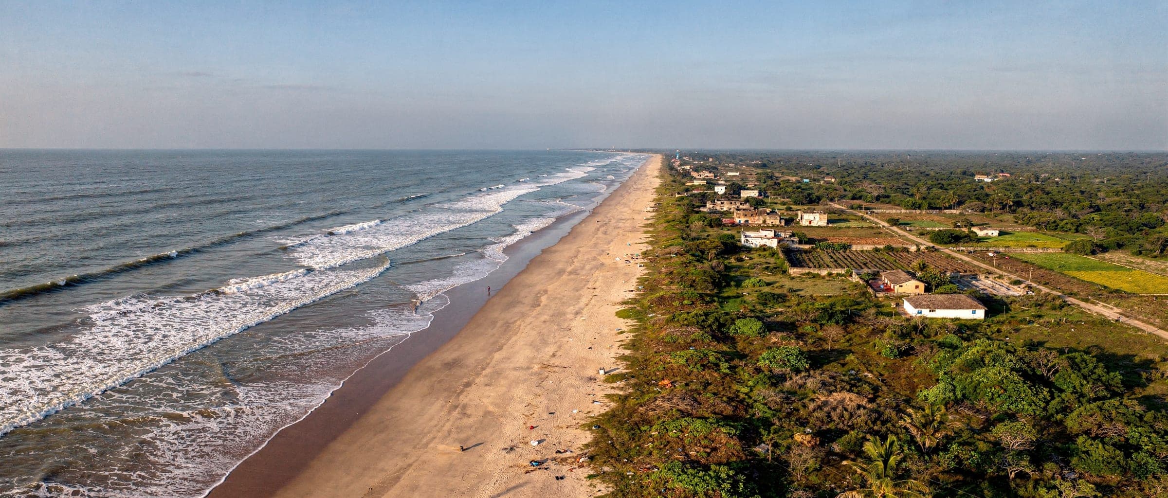 The Kothapatnam coastline from the air: a long straight beach, white surf, and fields and village houses along the landward side.