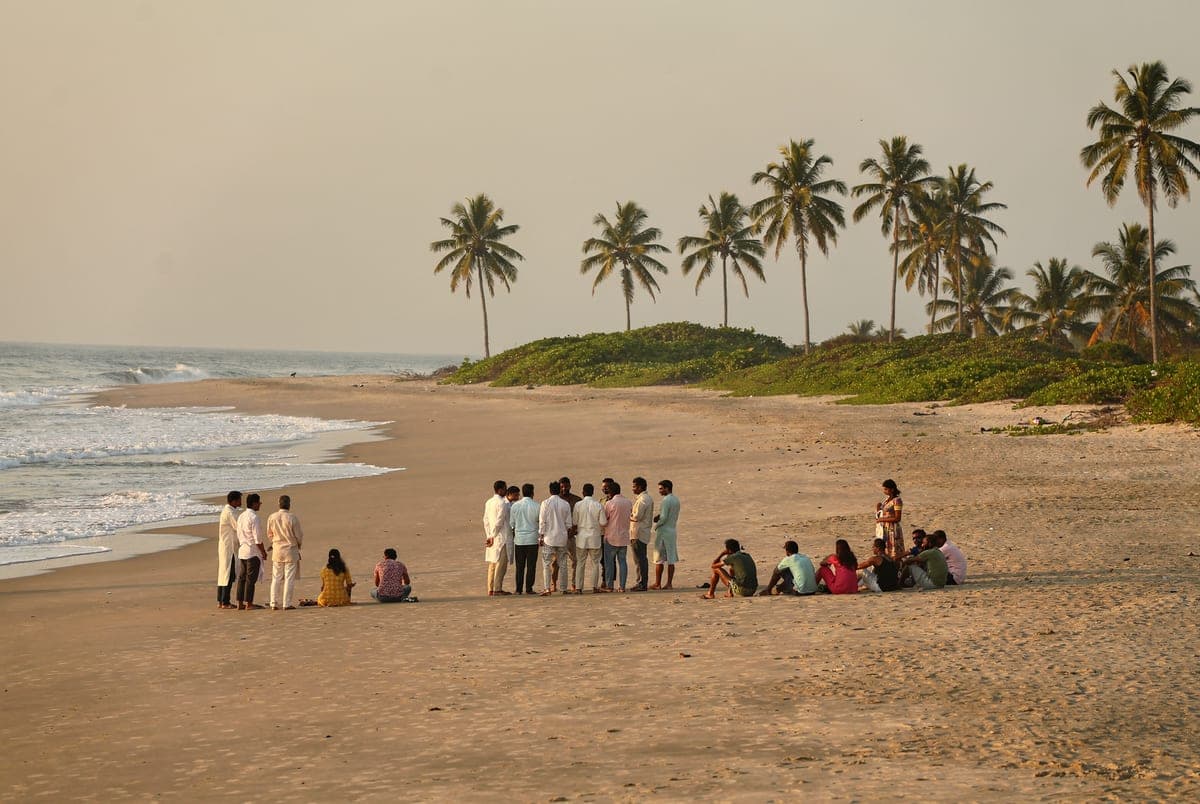 A company group spread out on the sand in the late afternoon, some standing in a circle and some sitting near the water.