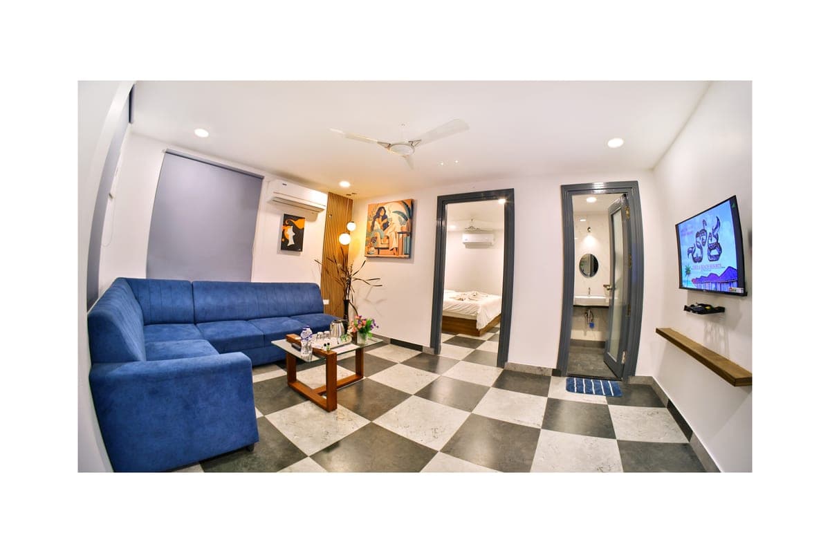 A Luxury Cottage seen across the living area, showing the blue corner sofa, the bedroom doorway, a marble washroom doorway and a wall-mounted television.