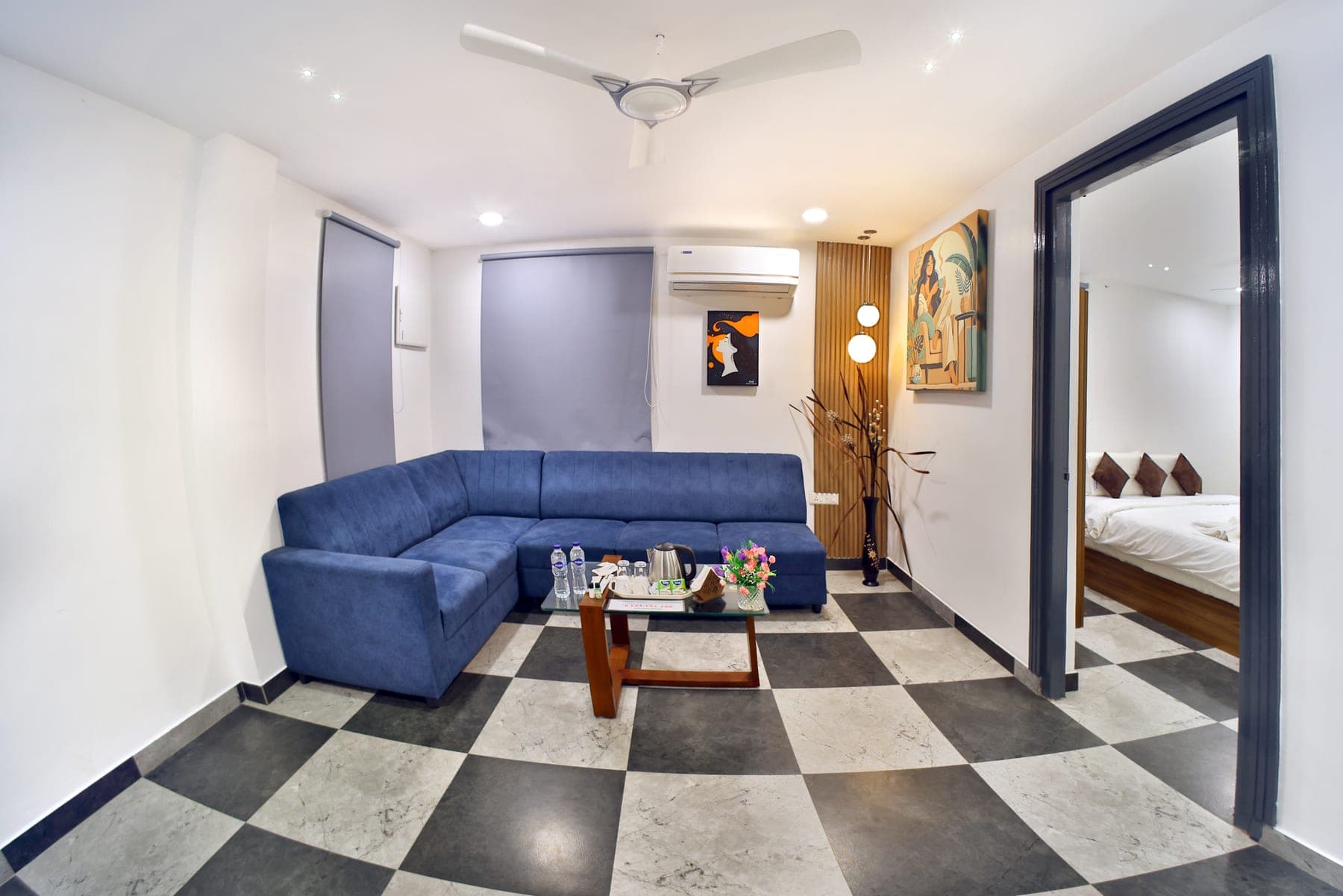 The living area of a Luxury Cottage: a large blue five-seater corner sofa on a chequered stone floor, with an archway through to the bedroom.