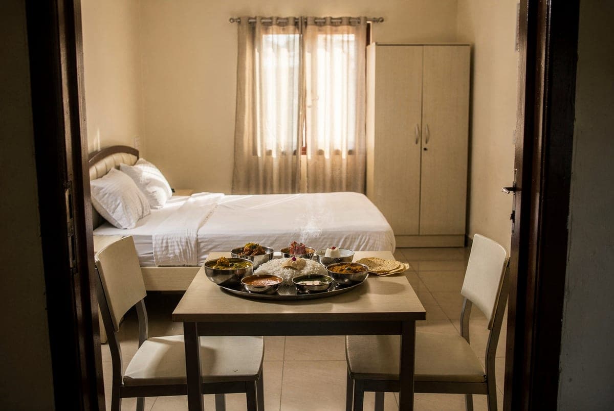 A South Indian thali and steel serving bowls laid out on the table inside a cottage, seen from the open doorway.