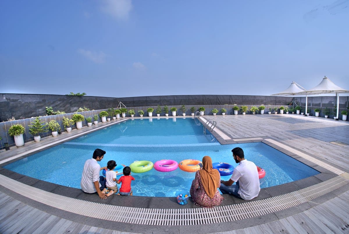 A family at the edge of the pool on a bright afternoon, children beside a row of colourful inflatable rings in the water.